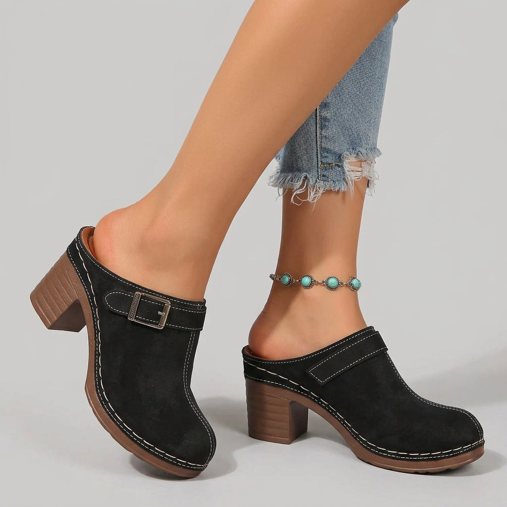 Black clogs with brown soles worn on a mosaic tile floor.
